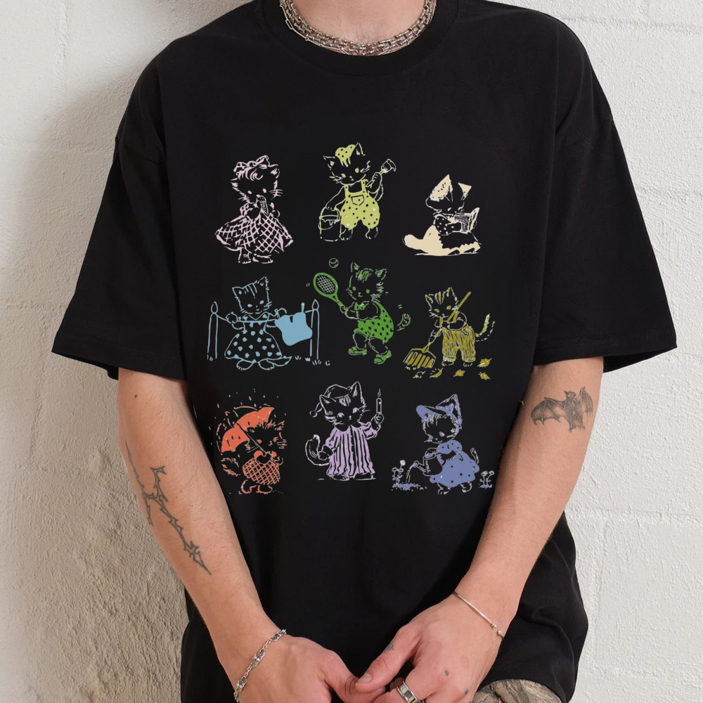 Black t-shirt with colorful cat illustrations worn by a person against a white wall.