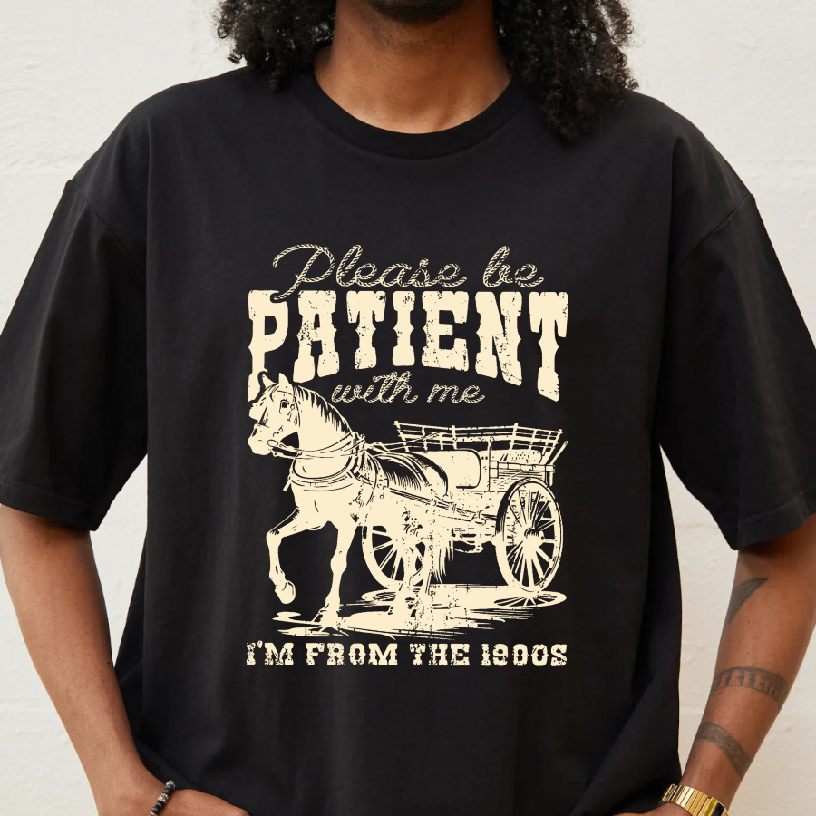 Black t-shirt with a graphic of a horse and carriage and text 'Please be patient with me I'm from the 1900s' worn by a person.