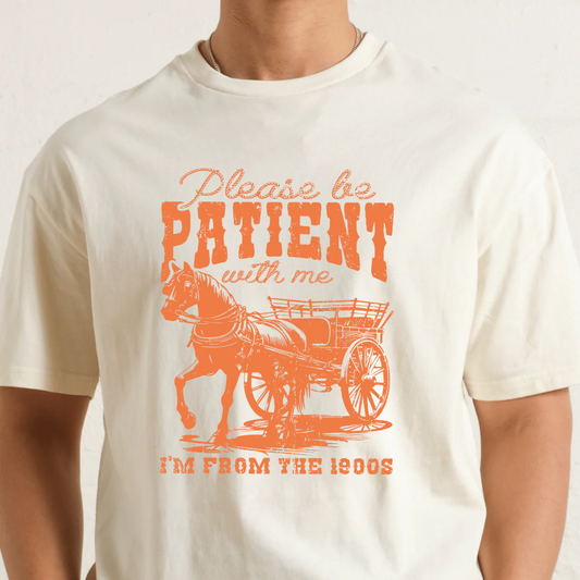Natural t-shirt with orange graphic and text 'Please be patient with me, I'm from the 1900s' on a plain background