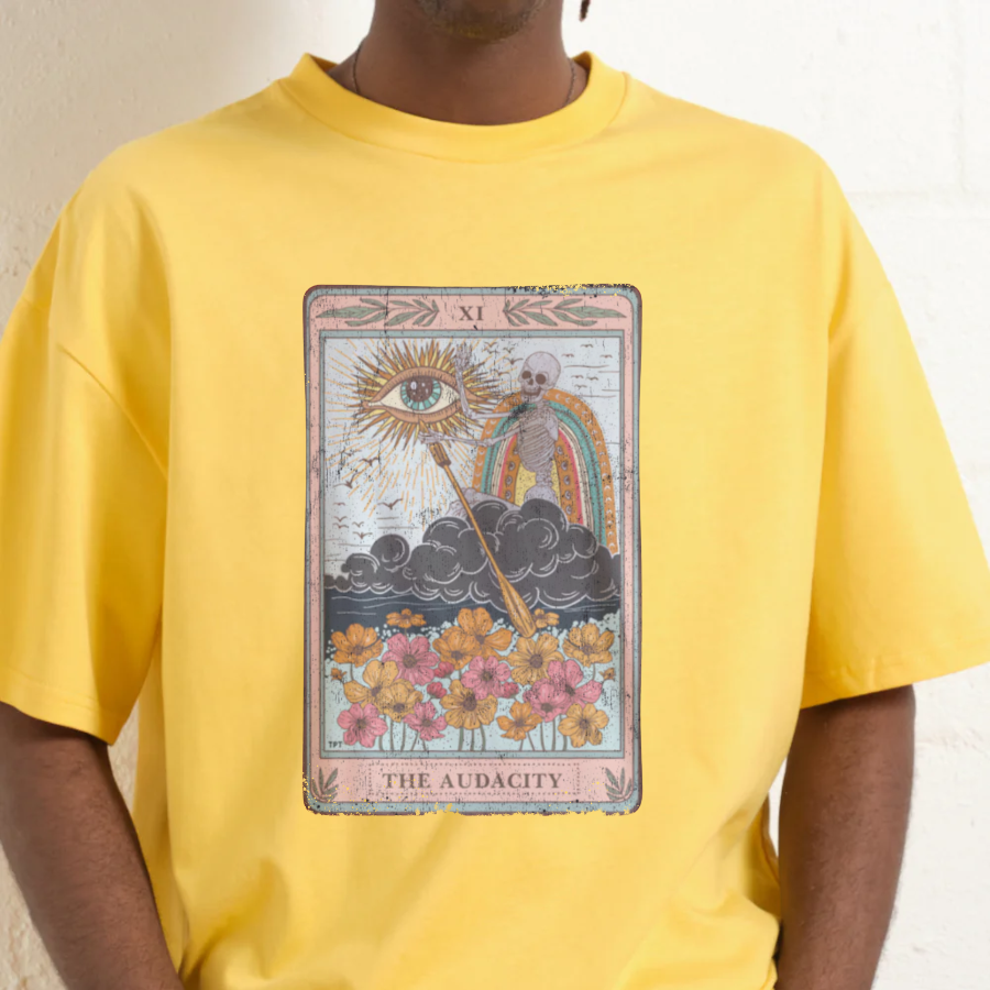 Person wearing a yellow t-shirt with 'The Audacity' tarot card design.