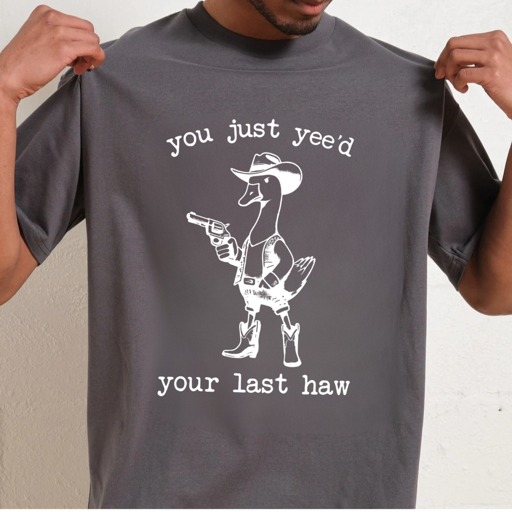 Person wearing a gray t-shirt with a graphic of a duck in a cowboy outfit and text.