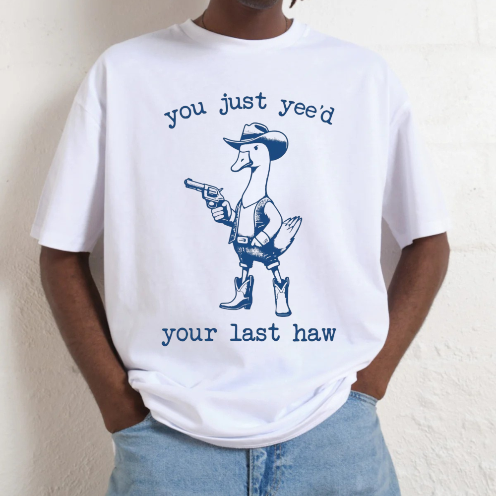 White t-shirt with a graphic of a duck wearing a cowboy hat and boots, holding a gun, with text 'you just yee'd your last haw' on a plain background.