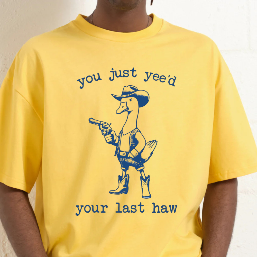 Yellow t-shirt with a graphic of a duck in a cowboy hat and boots holding a gun, with text 'you just yee'd your last haw'.