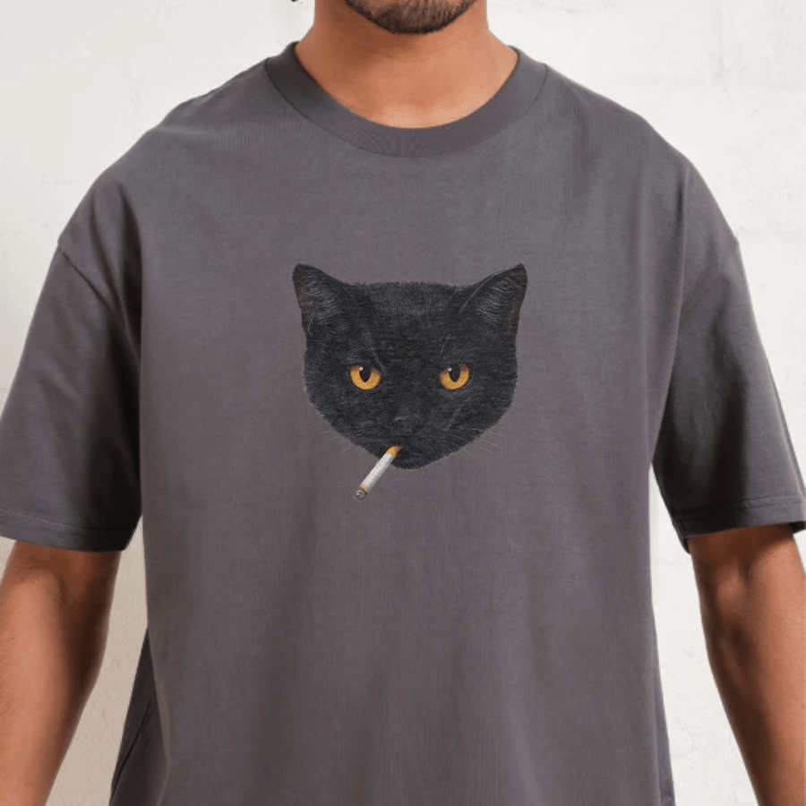 Person wearing a gray t-shirt with a black cat graphic holding a cigarette.