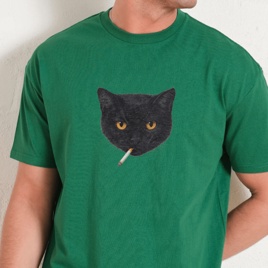 Green t-shirt with a black cat graphic holding a cigarette on a neutral background