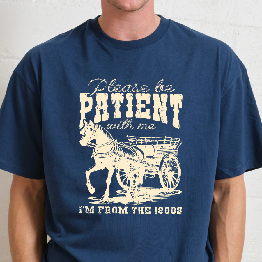 Navy blue t-shirt with a graphic of a horse and carriage and text 'Please be patient with me I'm from the 1800s' on a plain background.