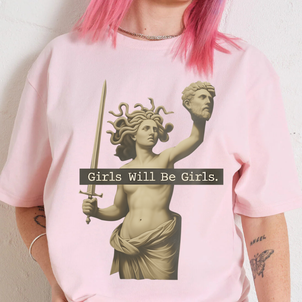 Person wearing a pink t-shirt with a graphic of a statue and 'Girls Will Be Girls' text.