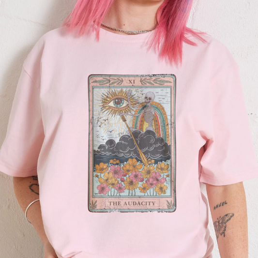Person wearing a pink t-shirt with a tarot card design on a plain background