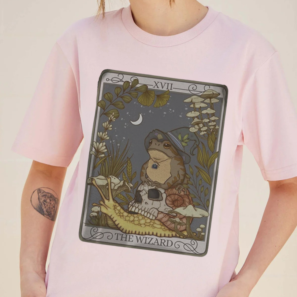Person wearing a pink t-shirt with a tarot card design featuring a frog labeled 'The Wizard'.