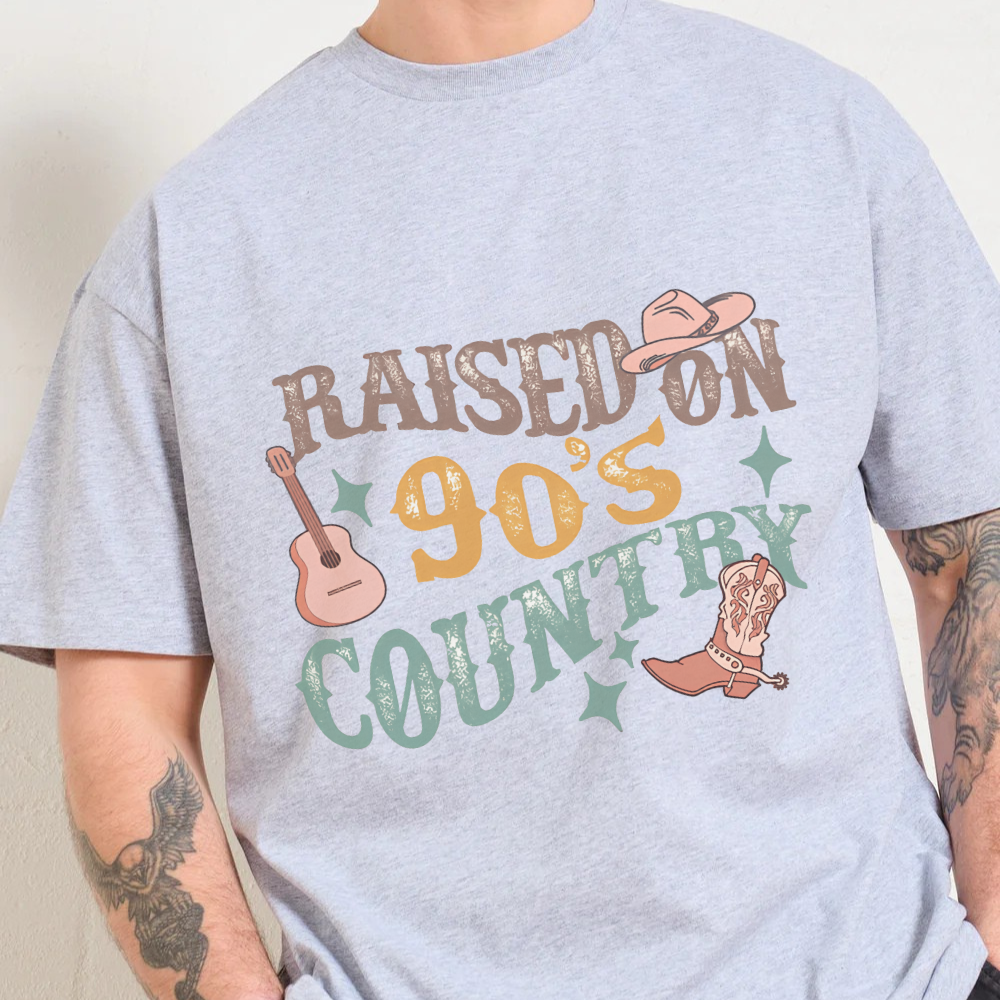 Gray t-shirt with 'Raised on 90's Country' graphic design featuring a guitar, cowboy hat, and boot.