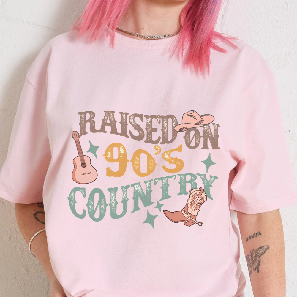 Person wearing a pink t-shirt with 'Raised on 90's Country' text and graphics.