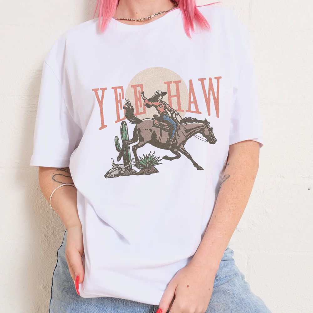 Person wearing a white t-shirt with a graphic design of a cowgirl on a horse and 'Yee Haw' text.