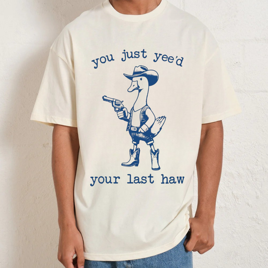 Person wearing a t-shirt with a graphic of a duck in cowboy attire and text.